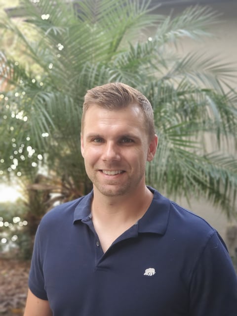 Mark Peterson, US Army Veteran founder of VetBenefitsGuide.org, smiling in front of tropical plants with string lights